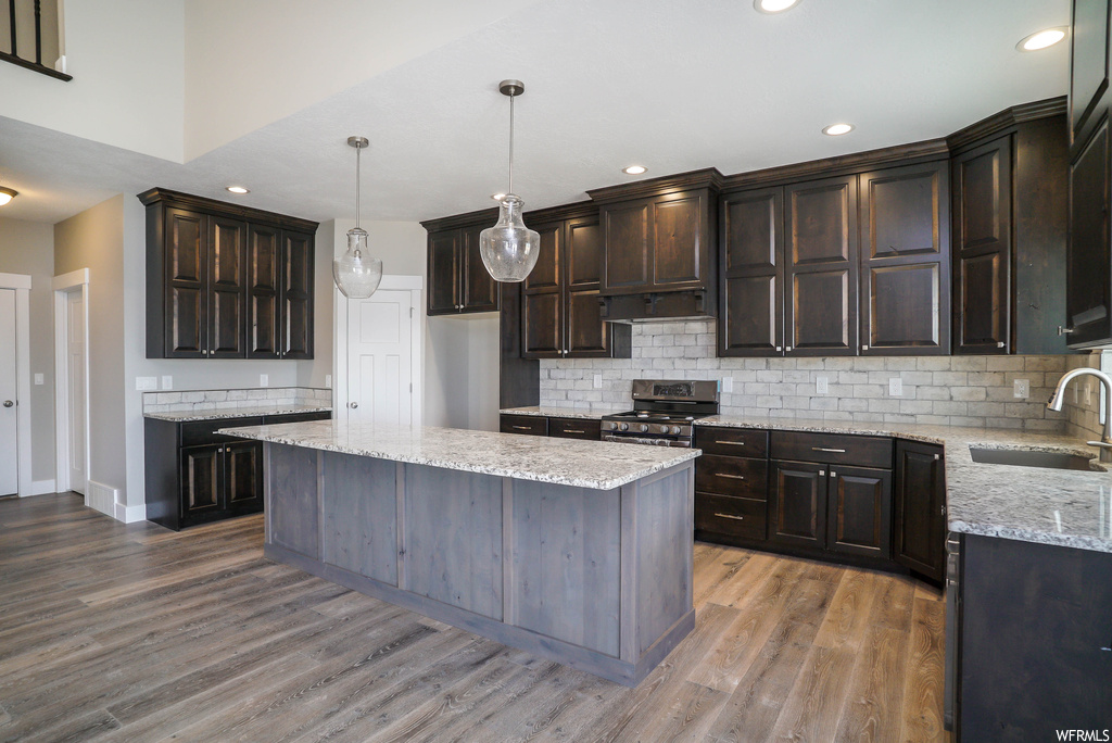 Kitchen featuring sink, light hardwood / wood-style flooring, a kitchen island, stainless steel range with gas cooktop, and pendant lighting