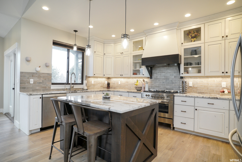Kitchen with stainless steel appliances, backsplash, light hardwood / wood-style flooring, and custom exhaust hood