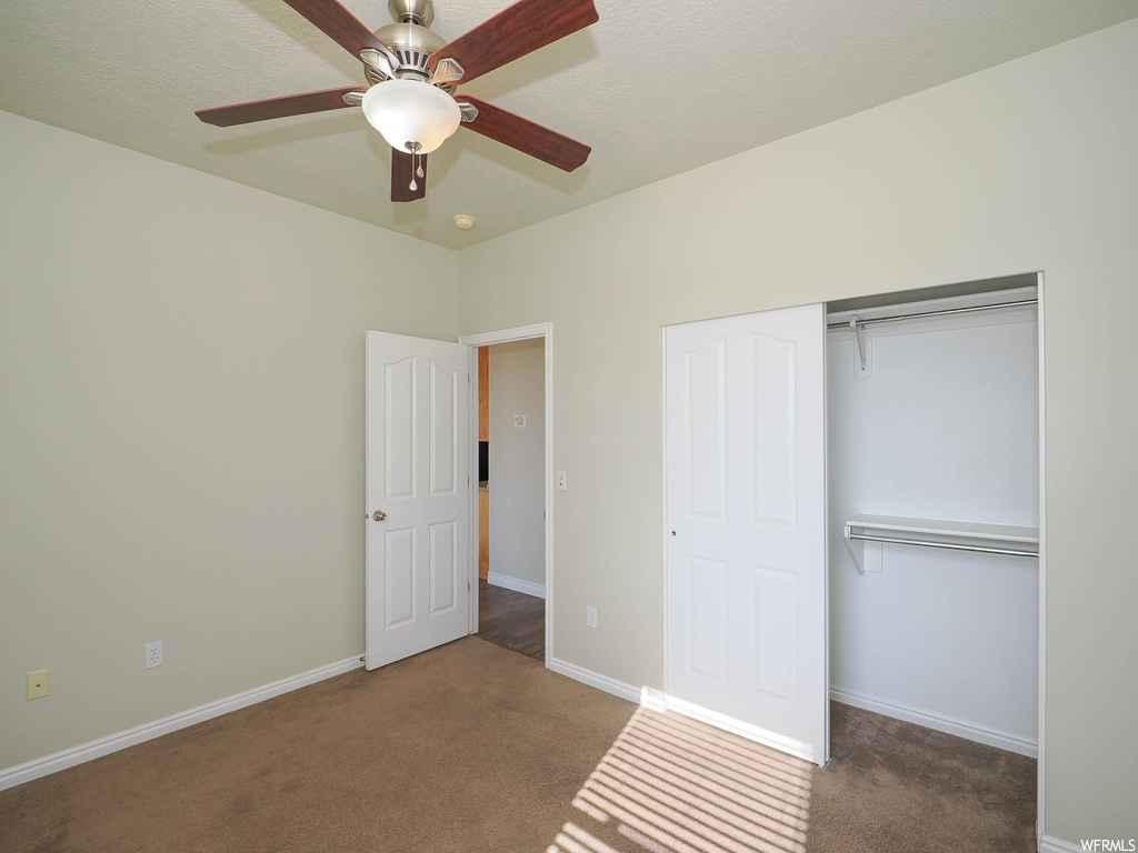 Unfurnished bedroom with a closet, ceiling fan, and dark colored carpet