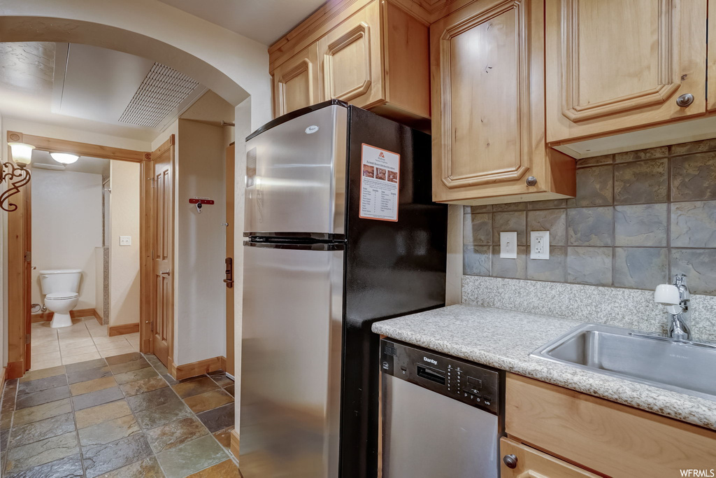 Kitchen with sink, backsplash, light tile floors, appliances with stainless steel finishes, and light brown cabinetry