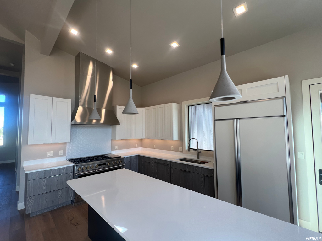 Kitchen featuring decorative light fixtures, dark wood-type flooring, sink, wall chimney range hood, and paneled built in fridge