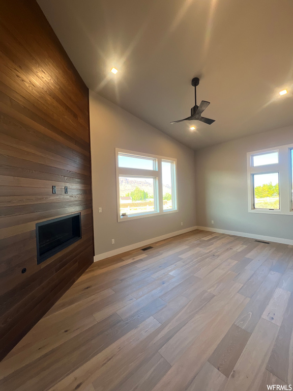 Unfurnished living room featuring light hardwood / wood-style floors, lofted ceiling, a fireplace, and ceiling fan
