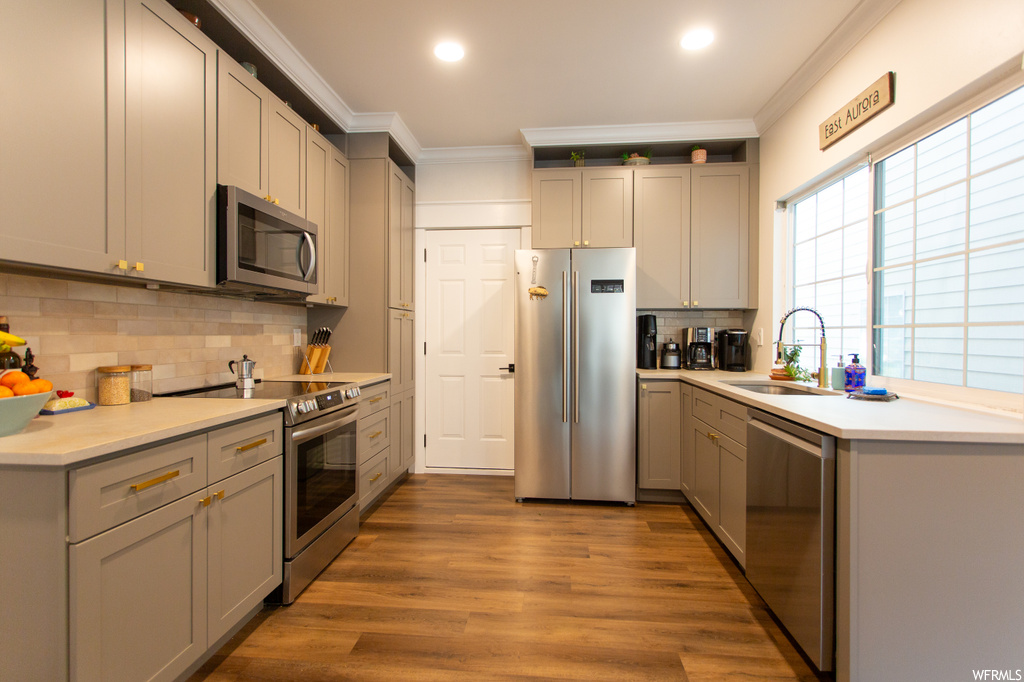 Kitchen featuring sink, crown molding, stainless steel appliances, hardwood / wood-style floors, and backsplash