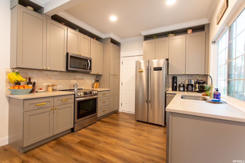 Kitchen with sink, crown molding, stainless steel appliances, backsplash, and light hardwood / wood-style flooring