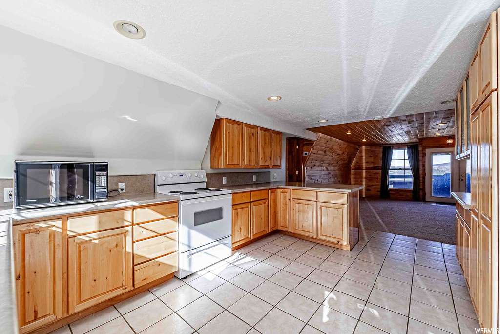 Kitchen with vaulted ceiling, light colored carpet, kitchen peninsula, and electric range