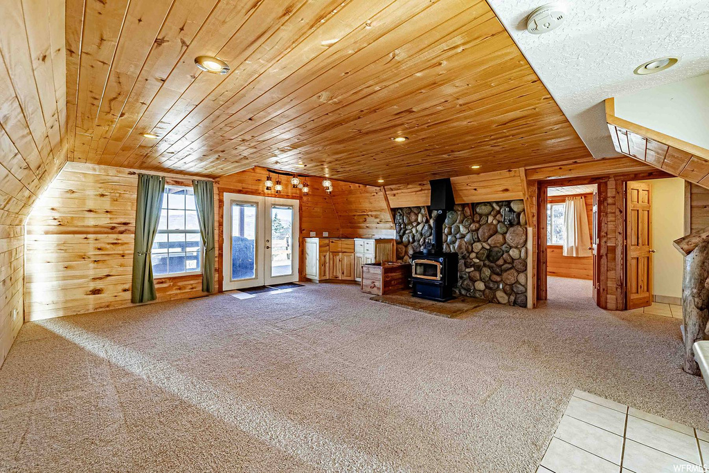 Unfurnished living room featuring light carpet, wood walls, lofted ceiling, a wood stove, and wooden ceiling