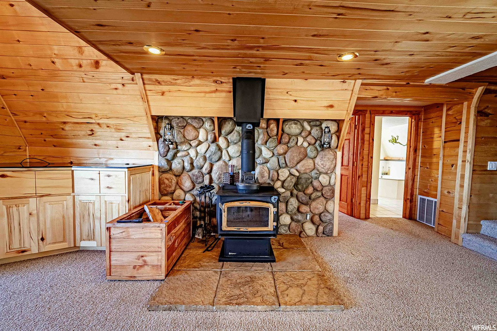 Carpeted living room featuring a wood stove, wood ceiling, and wood walls