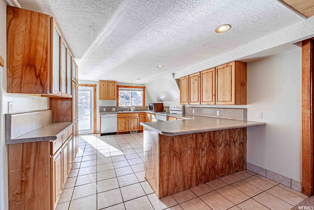 Kitchen with light tile flooring, white appliances, and kitchen peninsula