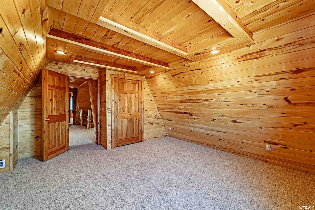 Additional living space with light colored carpet, wood walls, vaulted ceiling with beams, and wood ceiling