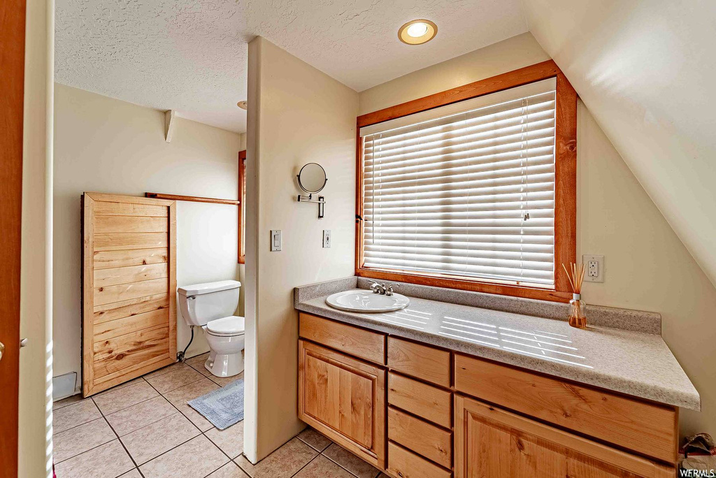 Bathroom with tile flooring, vanity, toilet, a textured ceiling, and lofted ceiling