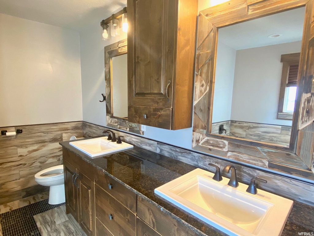 Bathroom with toilet, dual sinks, tile floors, large vanity, and tile walls