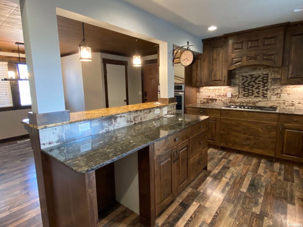 Kitchen with backsplash, dark hardwood / wood-style floors, dark stone counters, and appliances with stainless steel finishes
