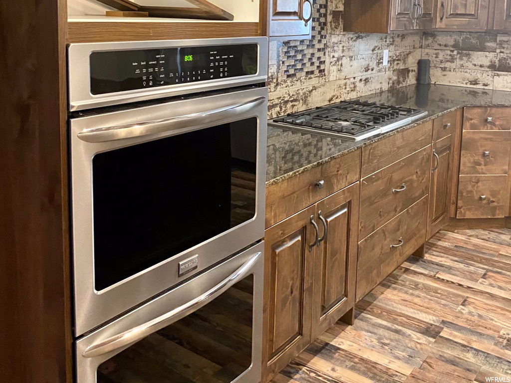 Kitchen featuring tasteful backsplash, dark stone counters, light hardwood / wood-style floors, custom exhaust hood, and stainless steel appliances
