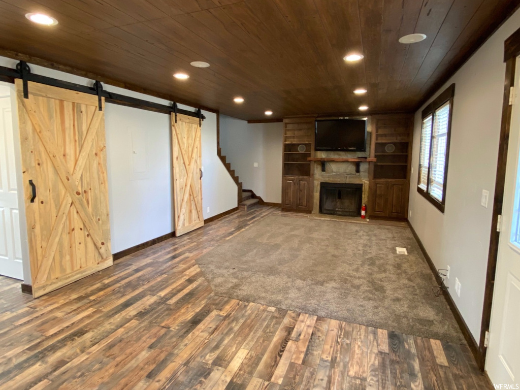 Unfurnished living room featuring wooden walls, a barn door, dark hardwood / wood-style flooring, and wooden ceiling