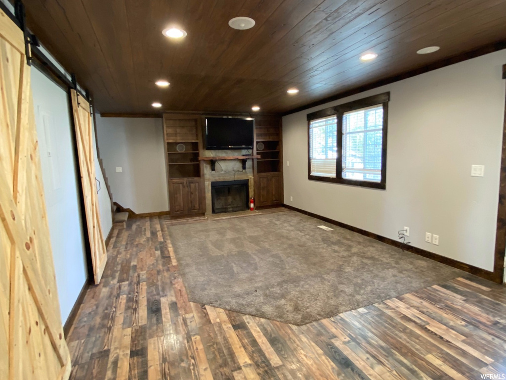 Unfurnished living room featuring a barn door, a fireplace, dark hardwood / wood-style floors, and wooden ceiling
