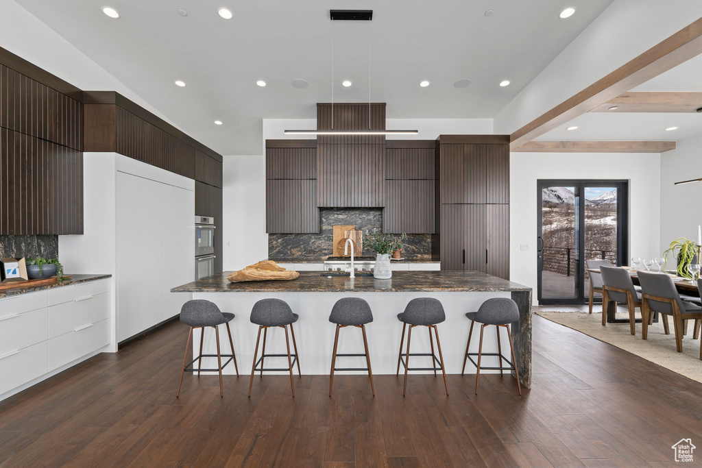 Kitchen featuring a breakfast bar area, dark hardwood / wood-style flooring, backsplash, and a kitchen island with sink