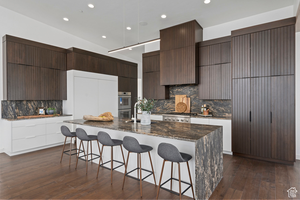 Kitchen featuring dark hardwood / wood-style floors, backsplash, and a kitchen island with sink