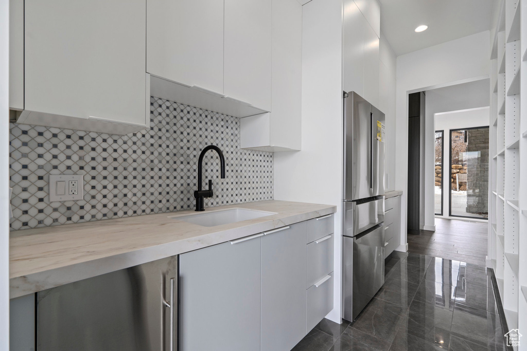 Kitchen featuring white cabinetry, dark tile flooring, sink, stainless steel refrigerator, and light stone counters