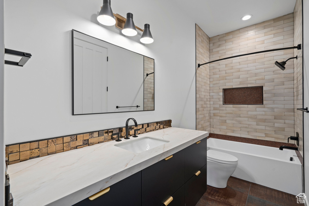 Full bathroom with vanity with extensive cabinet space, tiled shower / bath, toilet, tile flooring, and backsplash