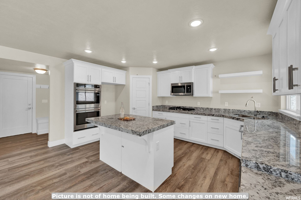 Kitchen with sink, light stone countertops, light wood-type flooring, white cabinetry, and stainless steel appliances