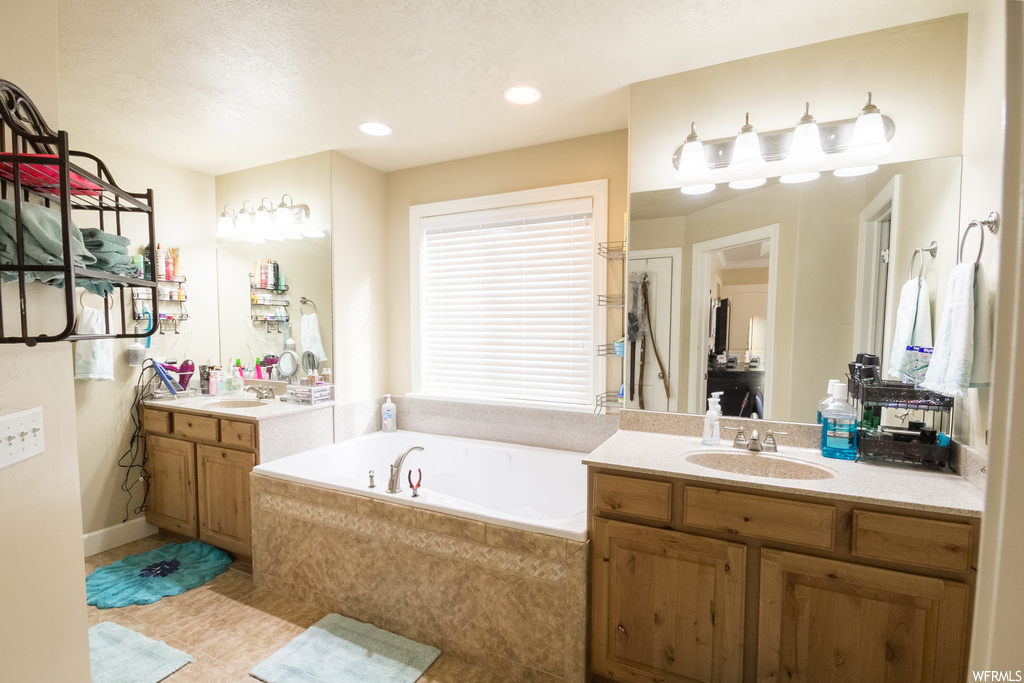 Bathroom featuring a textured ceiling, double sink vanity, tile flooring, and tiled bath