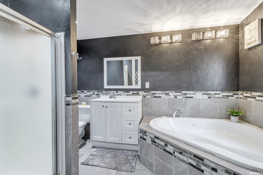 Bathroom featuring toilet, vanity, tiled tub, tile floors, and tile walls