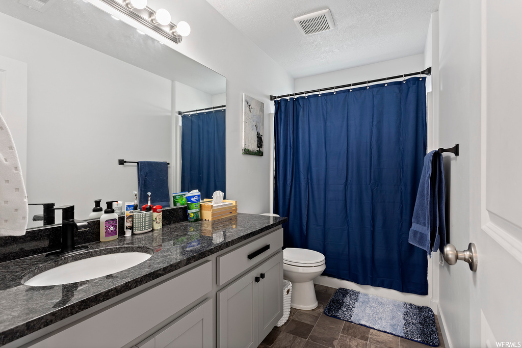 Bathroom featuring tile flooring, a textured ceiling, toilet, and oversized vanity
