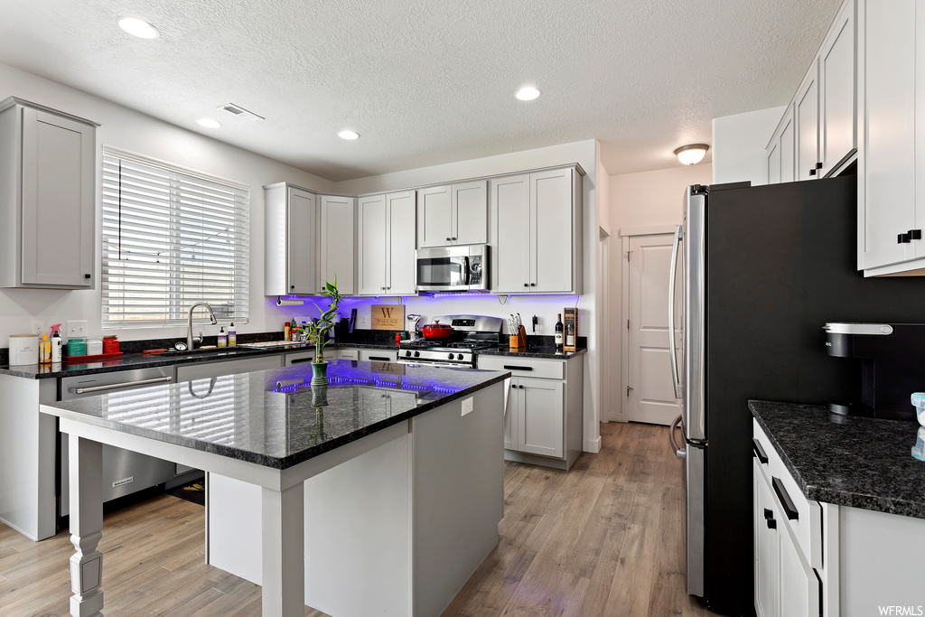 Kitchen featuring sink, a center island, dark stone countertops, and light hardwood / wood-style flooring