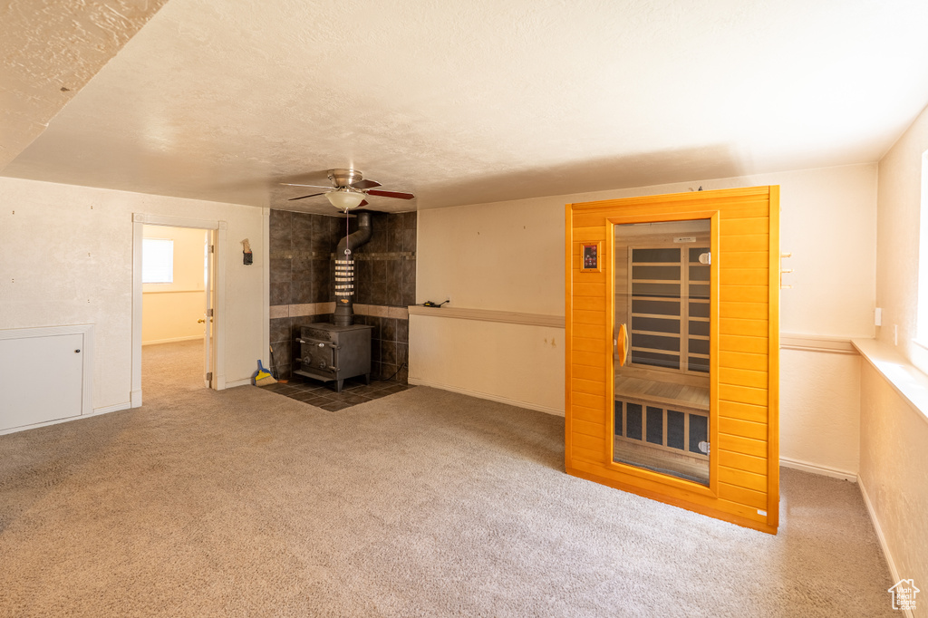 Unfurnished living room with a wood stove, a ceiling fan, baseboards, healthy amount of natural light, and a textured ceiling