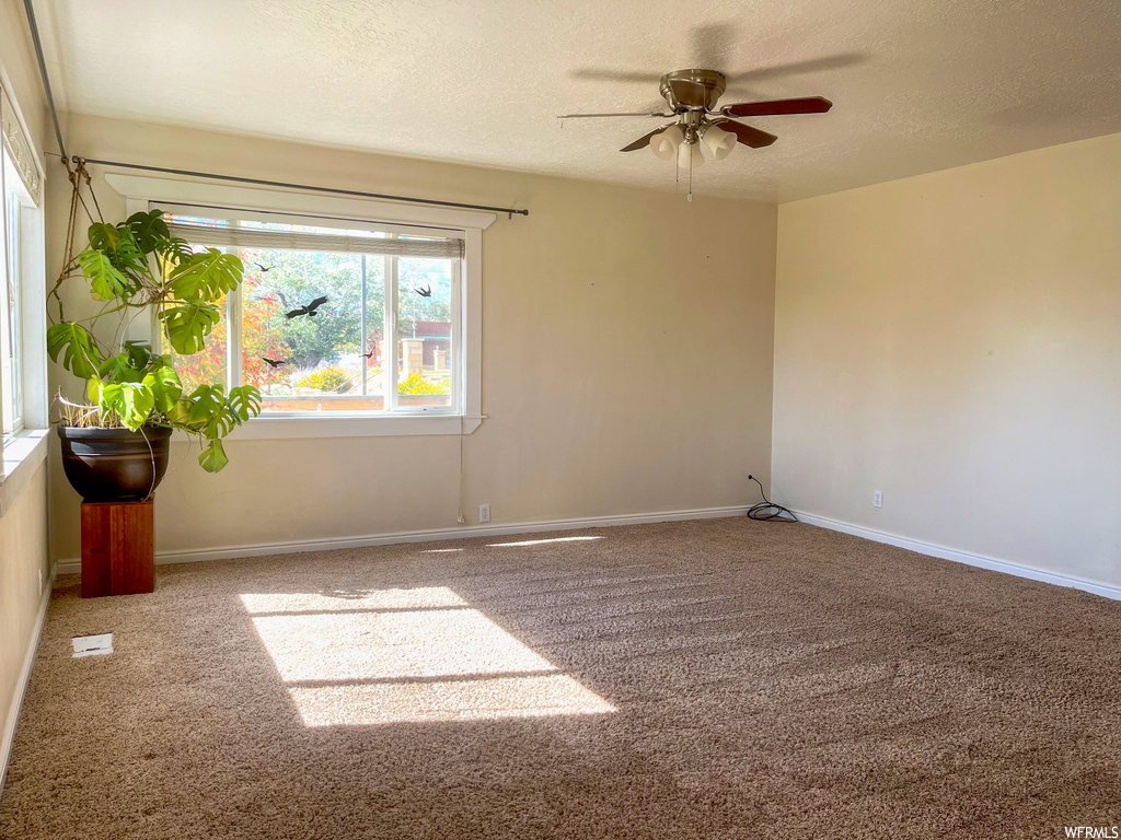 Empty room featuring a textured ceiling, ceiling fan, and carpet floors