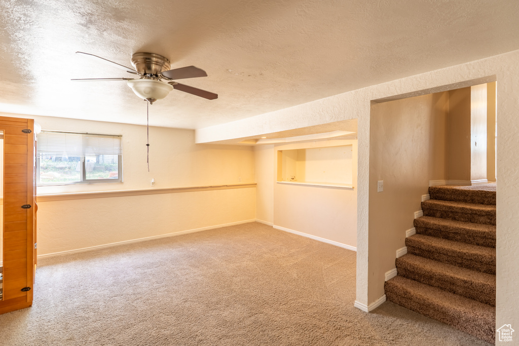 Carpeted spare room with a ceiling fan, stairway, baseboards, and a textured ceiling