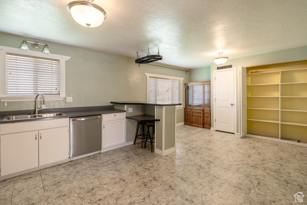 Kitchen with stainless steel dishwasher, a sink, a textured ceiling, dark countertops, and white cabinetry