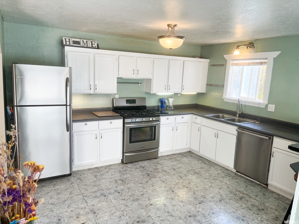 Kitchen featuring white cabinets, stainless steel appliances, light tile flooring, and sink