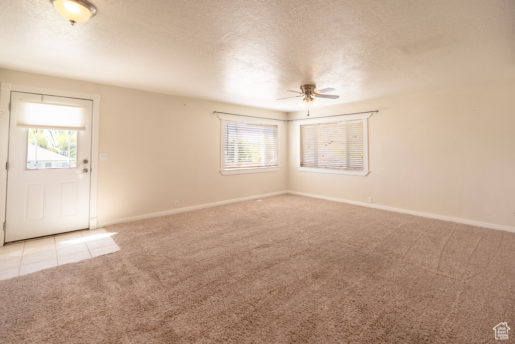 Spare room with light colored carpet, ceiling fan, a textured ceiling, plenty of natural light, and baseboards