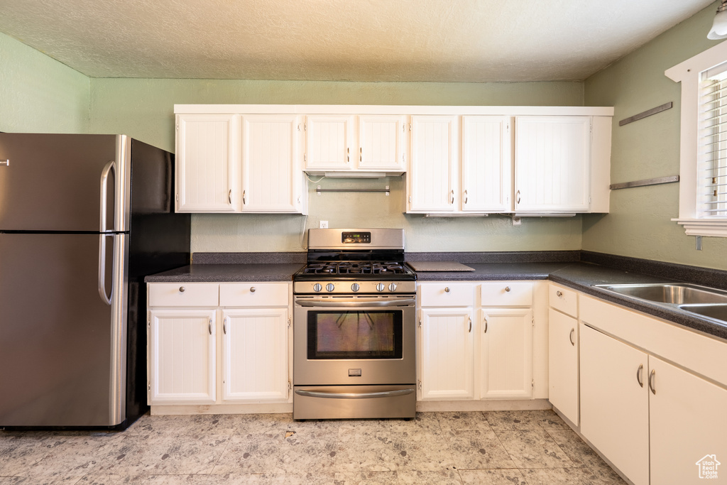 Kitchen with stainless steel appliances, dark countertops, a sink, and white cabinetry