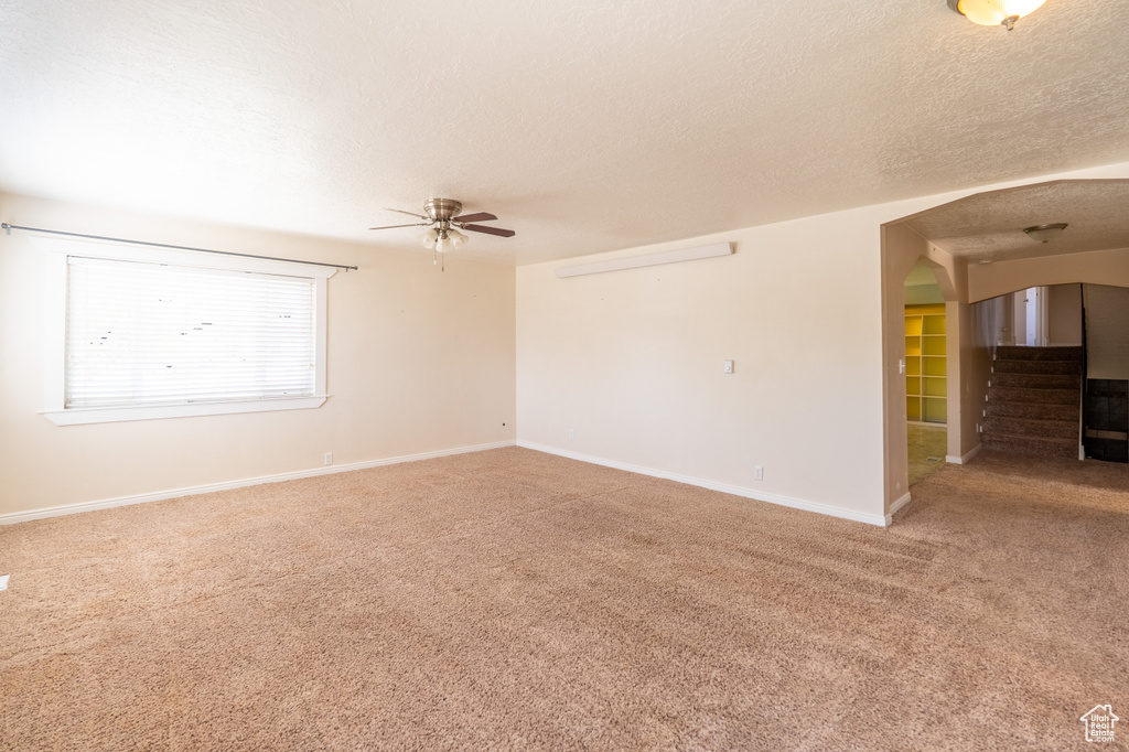 Empty room featuring light colored carpet, a ceiling fan, a textured ceiling, arched walkways, and baseboards
