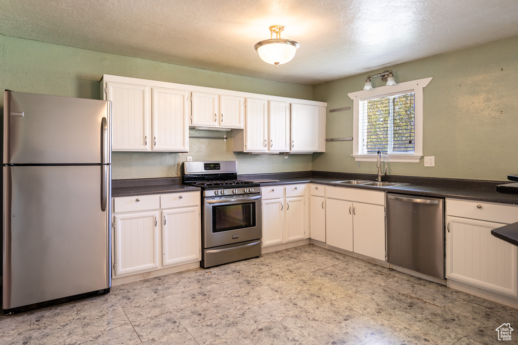 Kitchen featuring stainless steel appliances, a sink, dark countertops, a textured ceiling, and white cabinetry