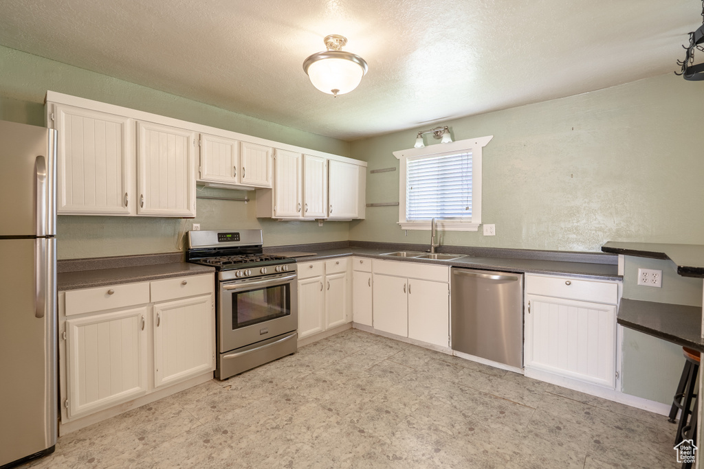 Kitchen featuring stainless steel appliances, a sink, dark countertops, white cabinets, and light flooring