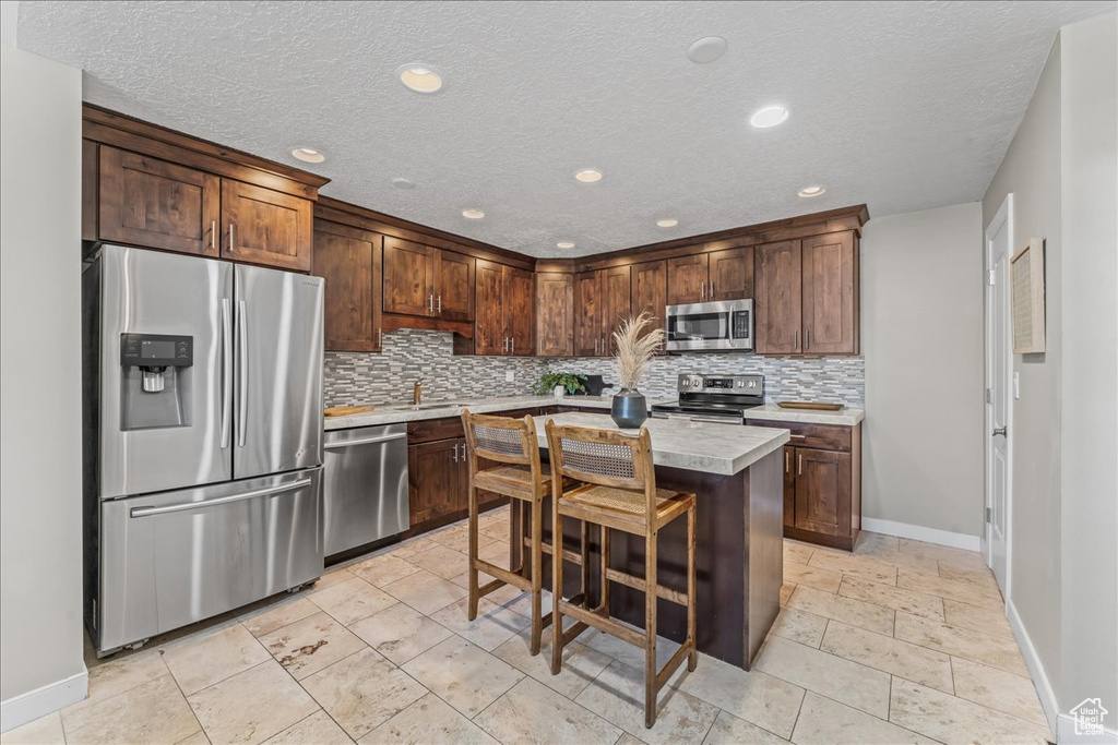 Kitchen featuring a kitchen island, appliances with stainless steel finishes, light tile floors, and tasteful backsplash