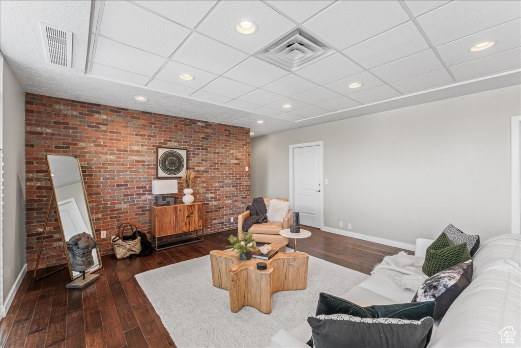 Living room with brick wall, dark wood-type flooring, and a paneled ceiling