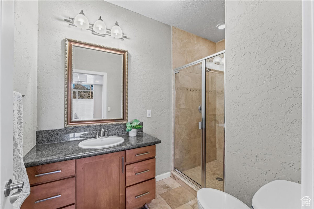 Bathroom with a textured ceiling, vanity with extensive cabinet space, walk in shower, toilet, and tile floors