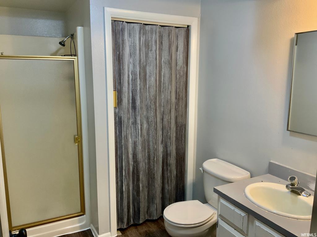 Bathroom with hardwood / wood-style flooring, an enclosed shower, large vanity, and toilet