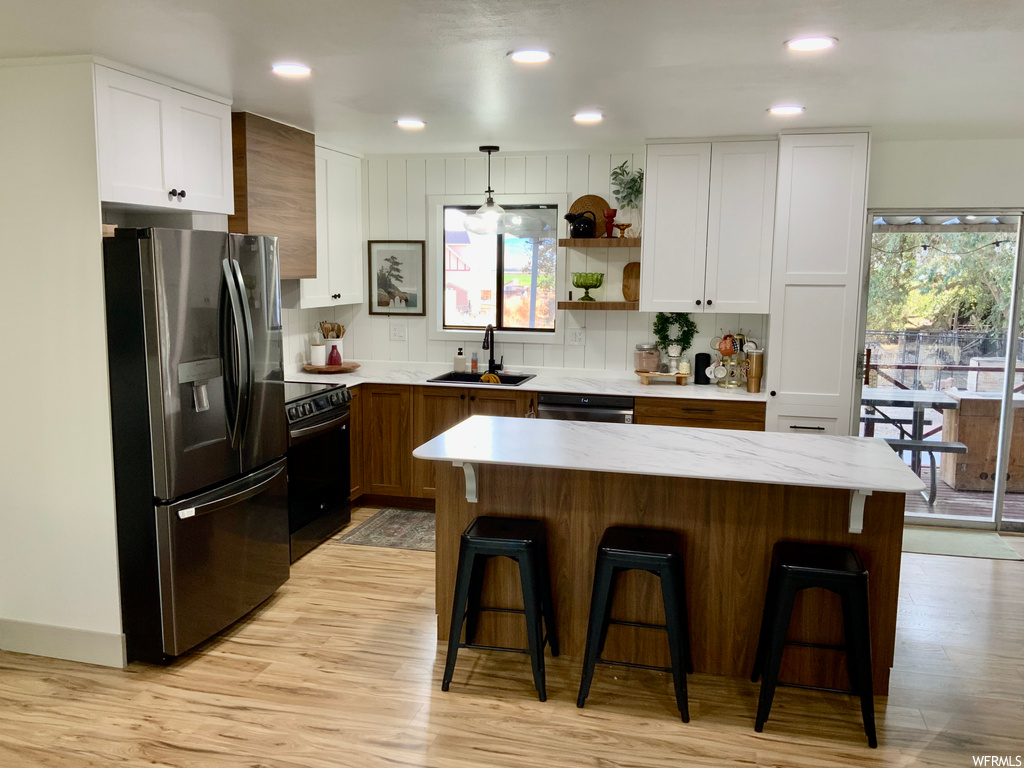Kitchen with plenty of natural light, stainless steel fridge with ice dispenser, decorative light fixtures, and white cabinets