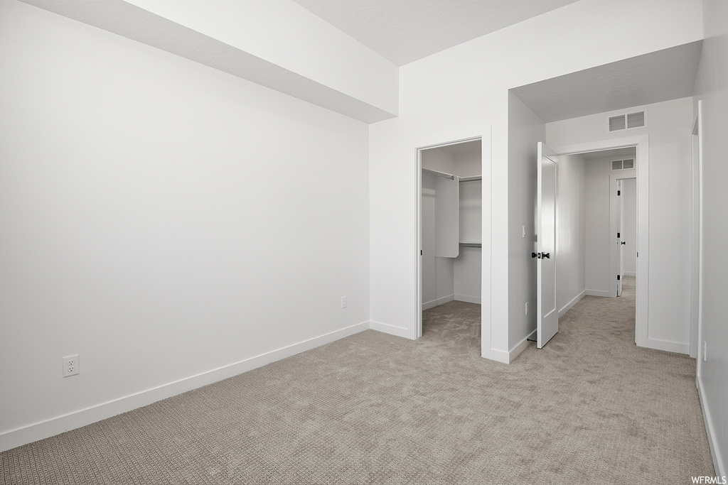 Unfurnished bedroom with light colored carpet, a closet, and a spacious closet