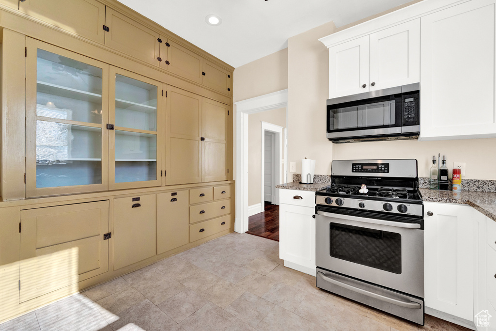 Kitchen with white cabinetry, stone countertops, appliances with stainless steel finishes, and light tile floors