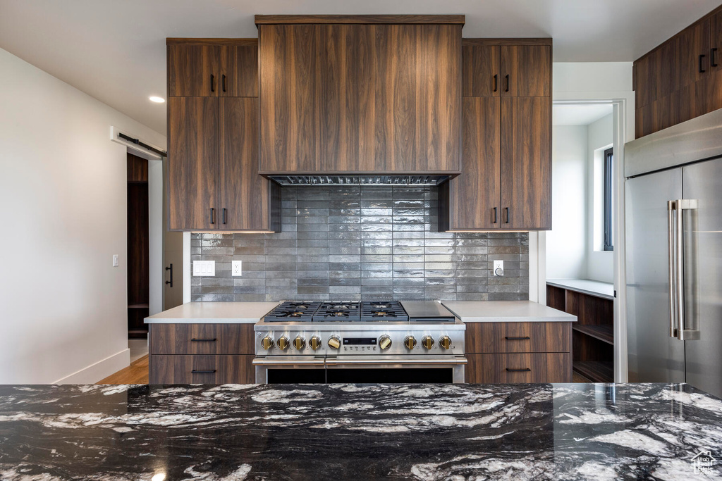 Kitchen with high quality appliances, tasteful backsplash, light wood-type flooring, and a barn door