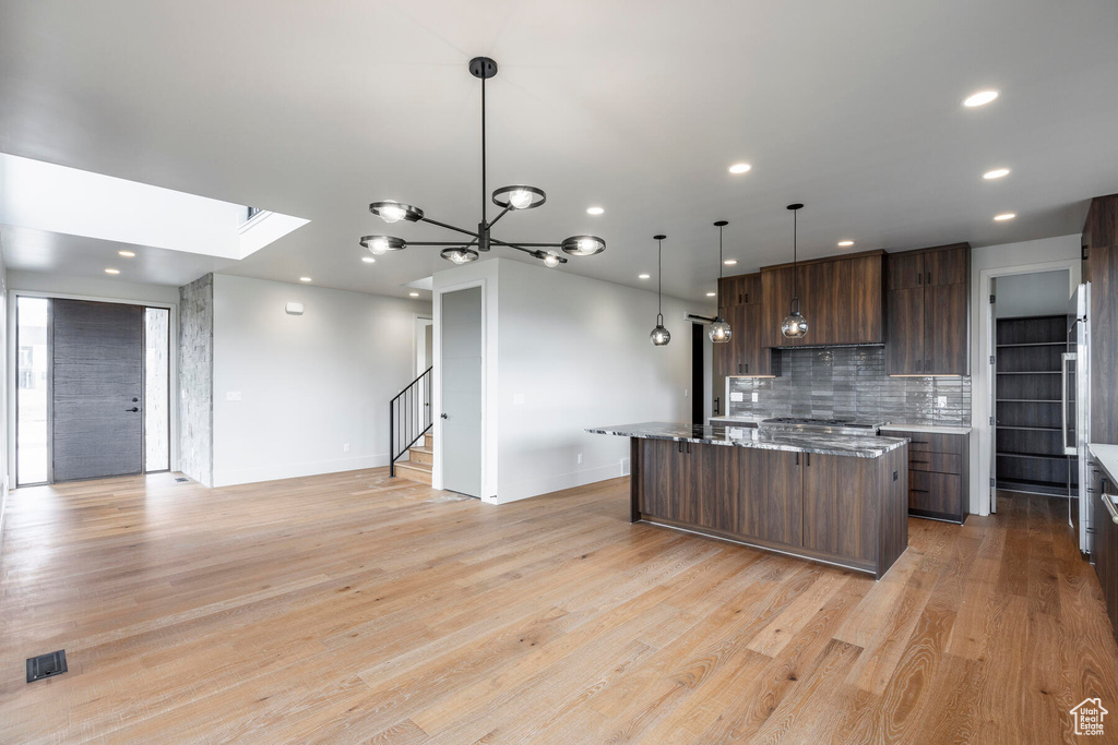 Kitchen featuring hanging light fixtures, light hardwood / wood-style flooring, tasteful backsplash, and a center island with sink