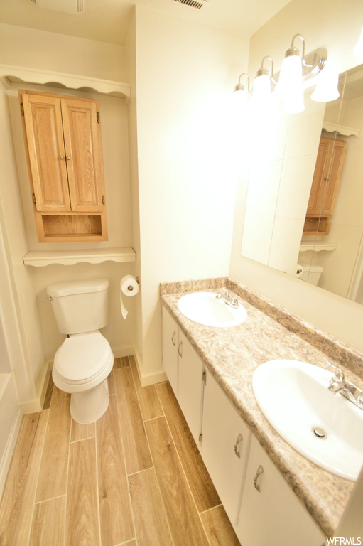 Bathroom with wood-type flooring, toilet, and double sink vanity