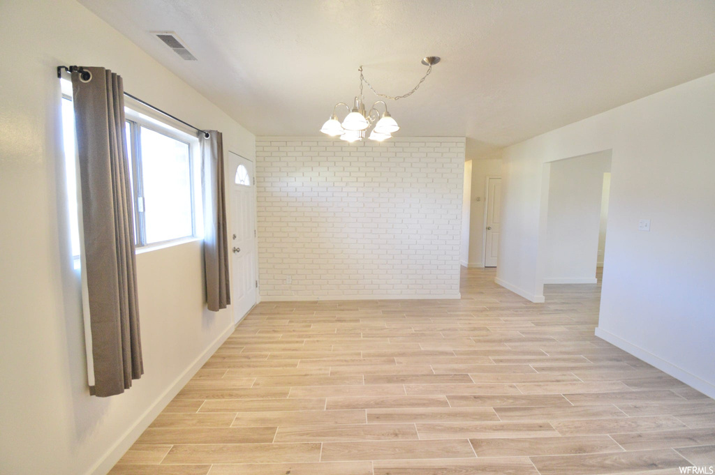 Empty room featuring brick wall, a notable chandelier, and light hardwood / wood-style flooring