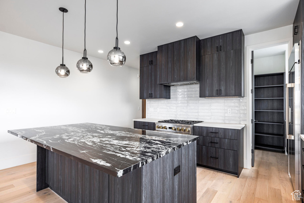 Kitchen with light hardwood / wood-style floors, hanging light fixtures, a center island, wall chimney range hood, and decorative backsplash